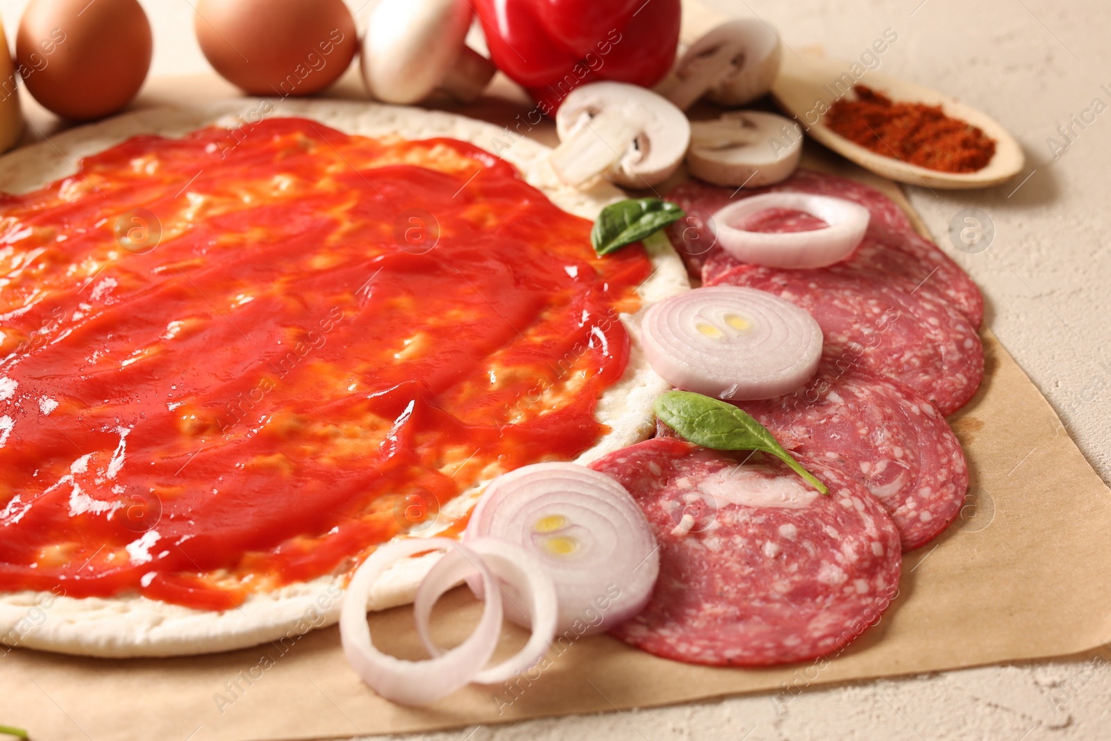 Photo of Pizza base smeared with tomato sauce and products on light textured table, closeup