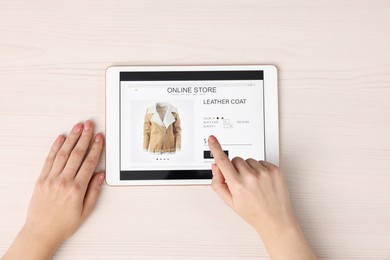 Woman with tablet shopping online at white wooden table, top view