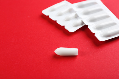 Suppositories on red background, closeup view. Hemorrhoid treatment