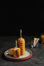 Plate with delicious grilled corn cobs on gray table against black background. Space for text