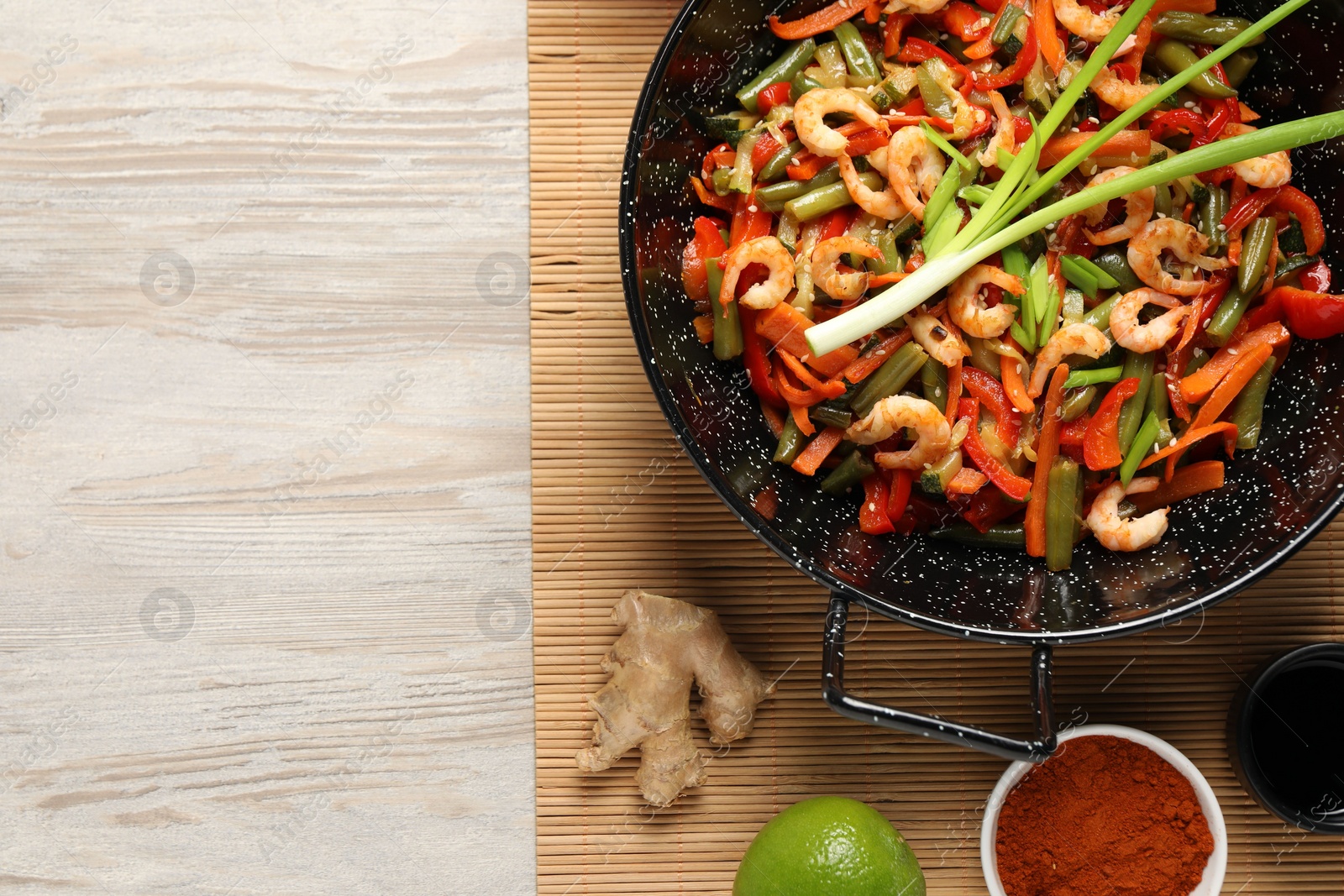 Photo of Shrimp stir fry with vegetables in wok and ingredients on wooden table, flat lay. Space for text