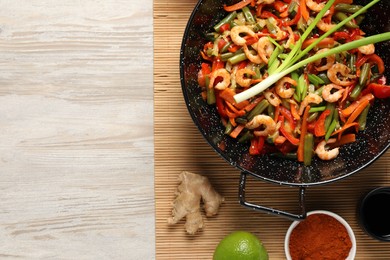 Shrimp stir fry with vegetables in wok and ingredients on wooden table, flat lay. Space for text