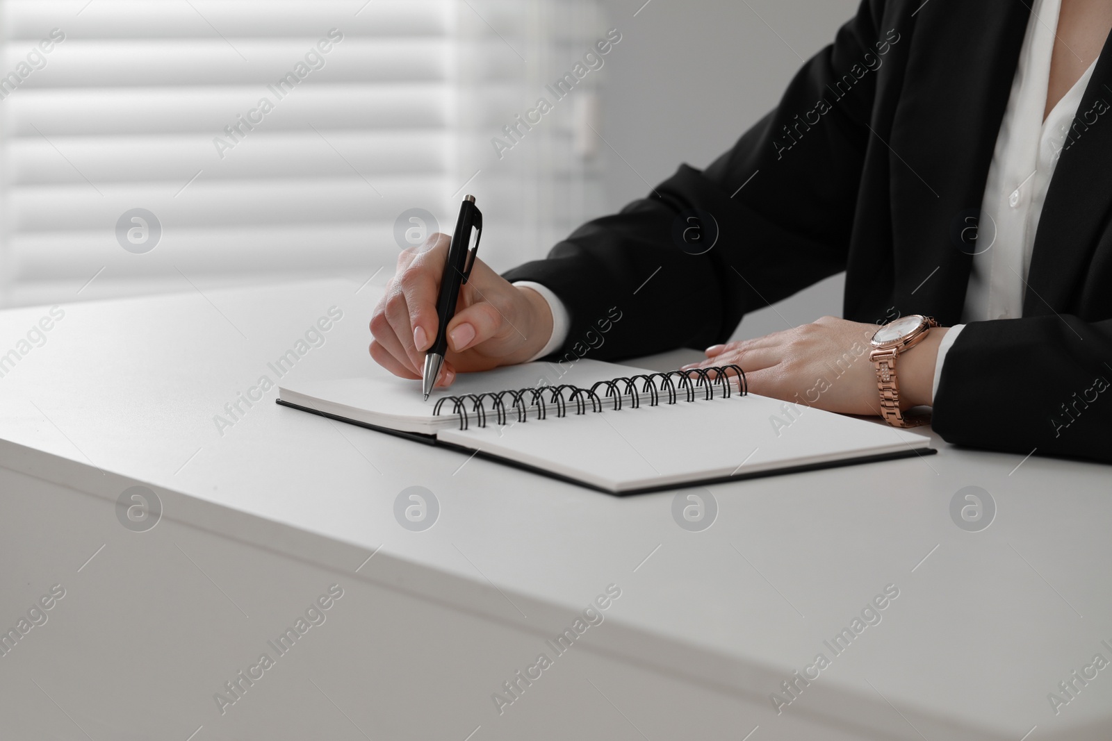 Photo of Woman writing in notebook at white table, closeup