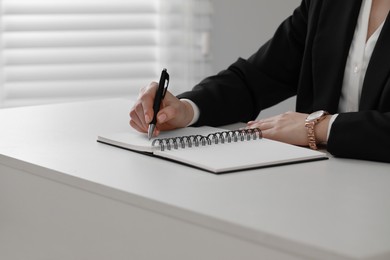 Photo of Woman writing in notebook at white table, closeup