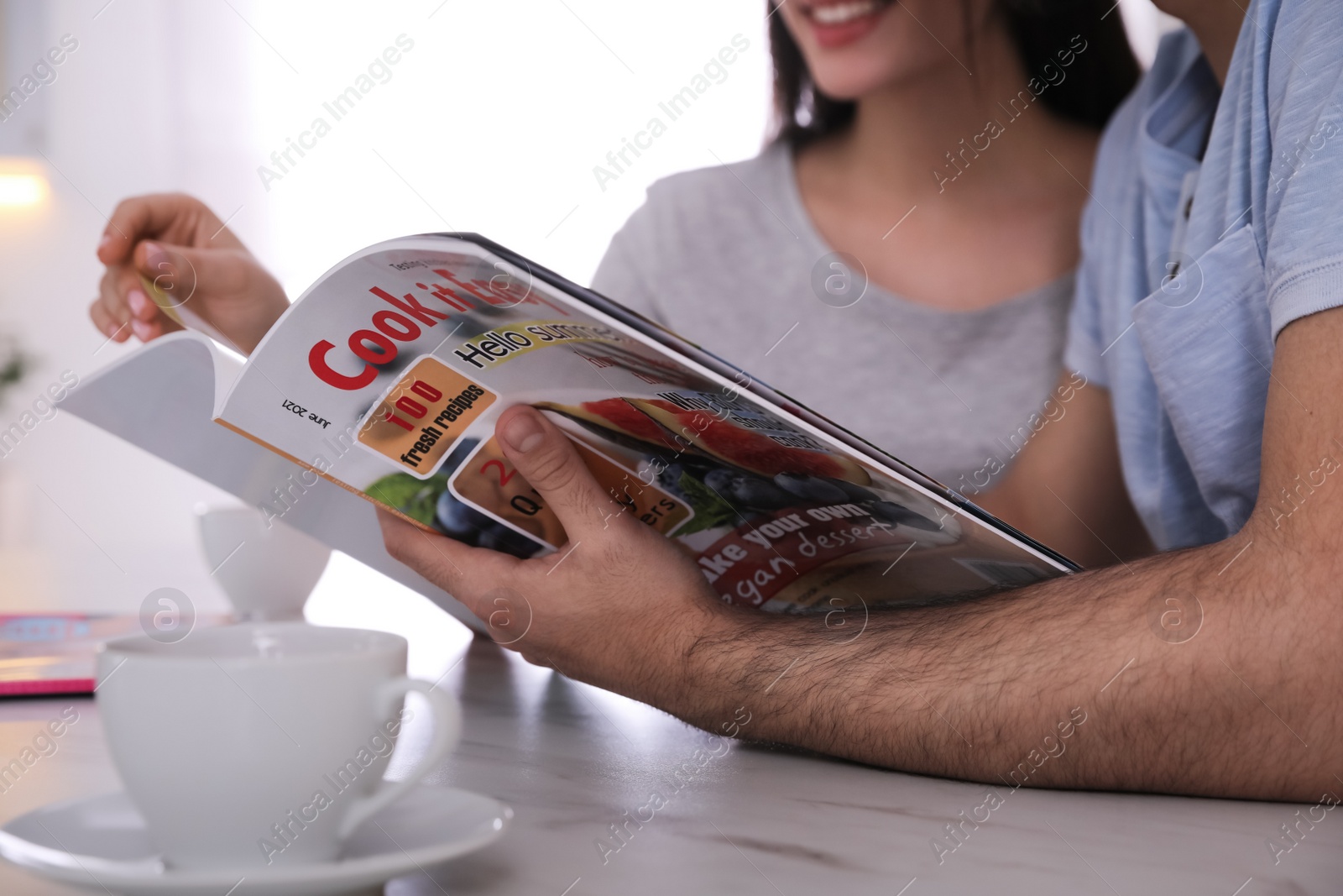 Photo of Couple reading magazine at table in kitchen, closeup