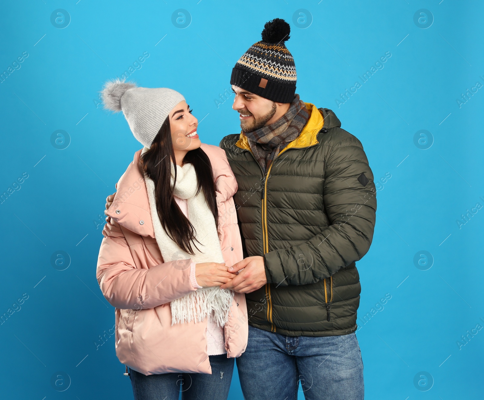 Photo of Happy young couple in warm clothes on blue background. Winter vacation