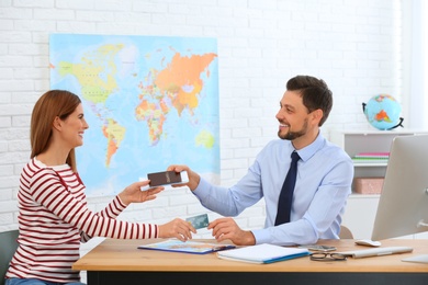 Male manager giving passport with ticket to client in travel agency