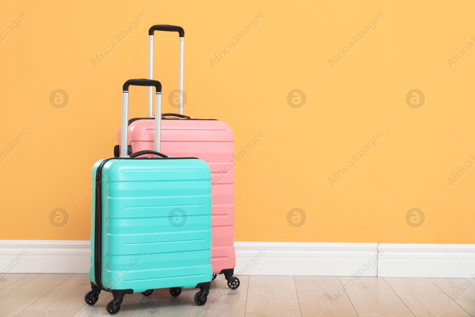 Photo of Suitcases packed for travel on floor near color wall. Space for text