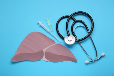 Photo of Paper liver, stethoscope, syringe and vial on light blue background, flat lay. Hepatitis treatment