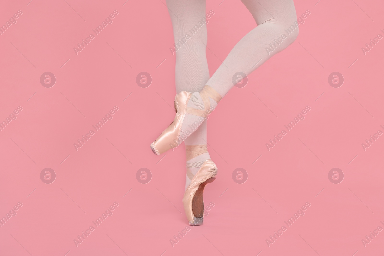 Photo of Young ballerina in pointe shoes practicing dance moves on pink background, closeup