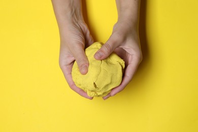 Woman playing with kinetic sand on yellow background, top view