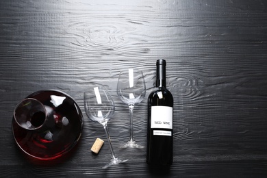 Decanter, glasses and bottle with red wine on wooden background, flat lay. Space for text