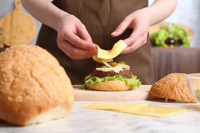 Photo of Woman making delicious vegetarian burger at white marble table, closeup