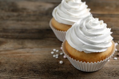 Delicious cupcakes with cream on wooden table, closeup. Space for text