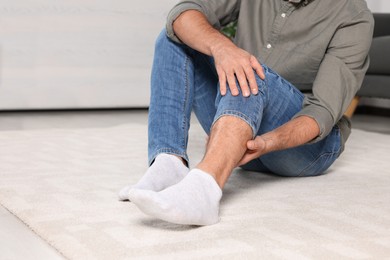 Photo of Man suffering from leg pain on white carpet indoors, closeup