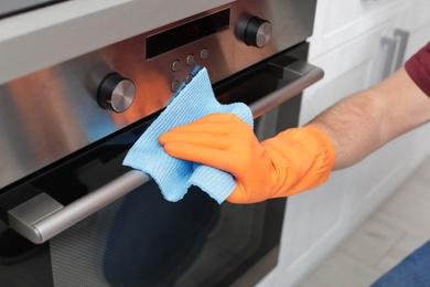 Young man cleaning oven with rag in kitchen, closeup