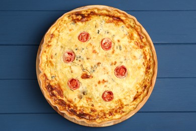 Photo of Delicious quiche with cheese and tomatoes on blue wooden table, top view