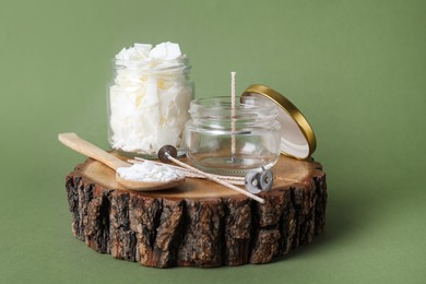 Ingredients for homemade candle on wooden stump against green background