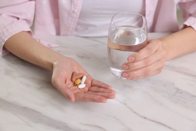 Photo of Woman with vitamin pills and glass of water at table indoors, closeup