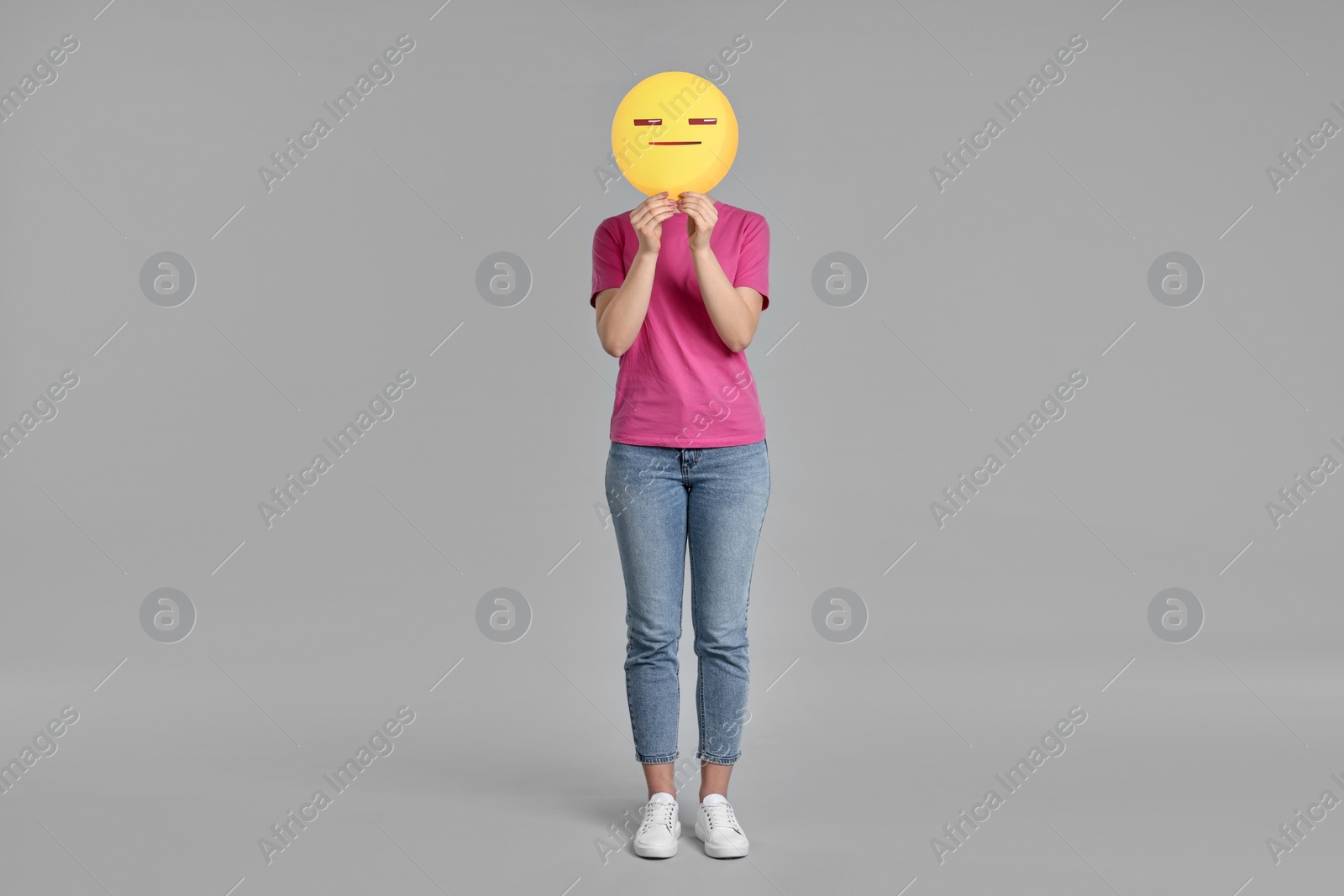 Photo of Woman holding emoticon with closed eyes and mouth on grey background. Space for text