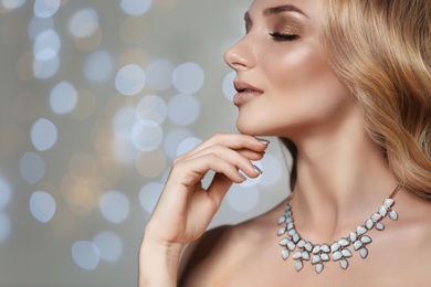 Photo of Beautiful young woman with elegant jewelry against defocused lights, closeup. Space for text