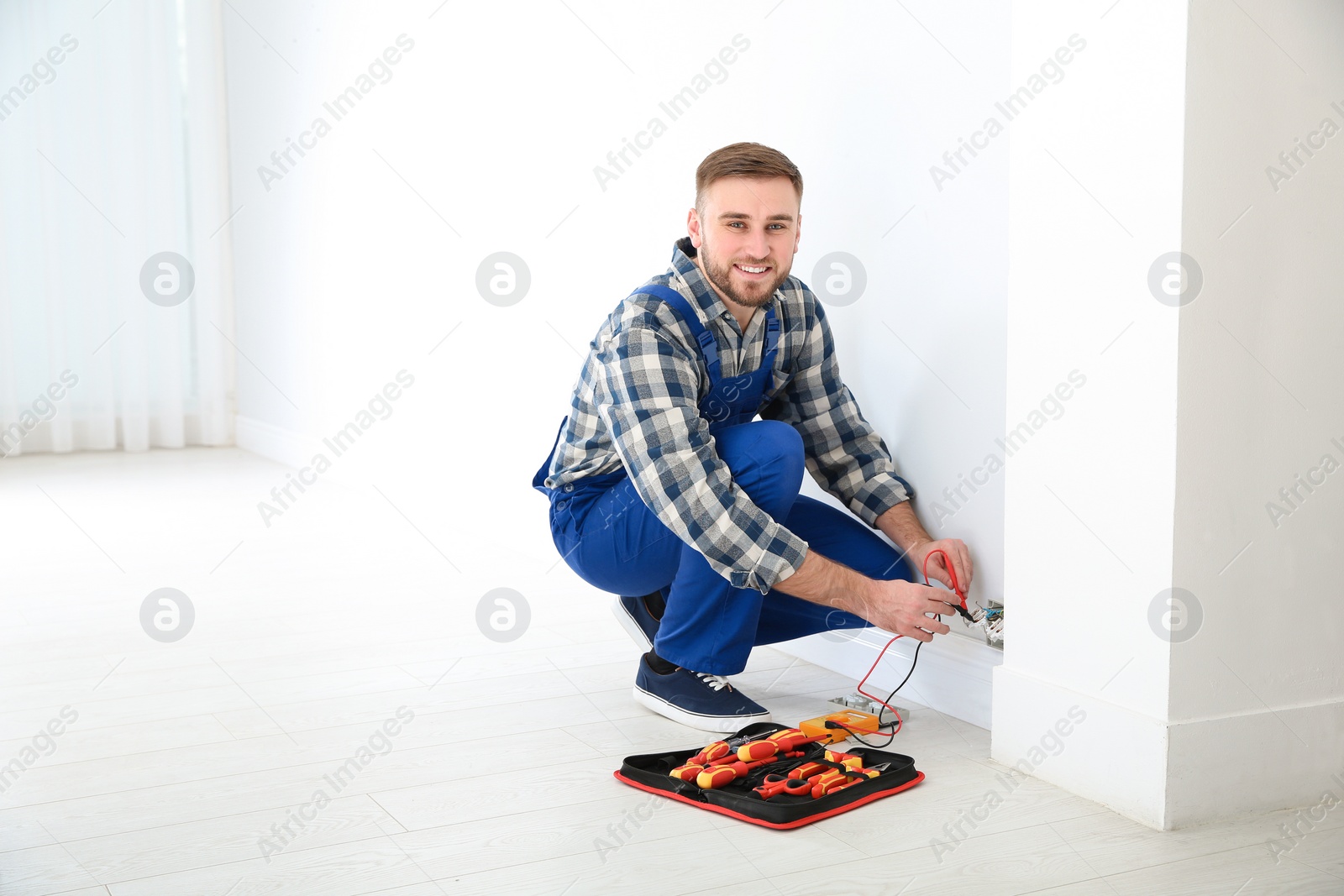 Photo of Professional electrician with tester checking voltage indoors, space for text