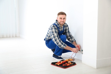 Professional electrician with tester checking voltage indoors, space for text