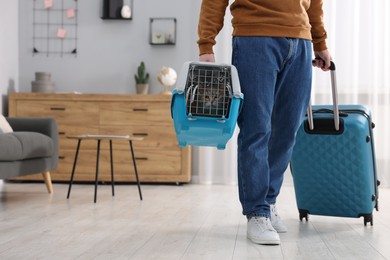 Travel with pet. Man holding carrier with cute cat and suitcase at home, closeup. Space for text