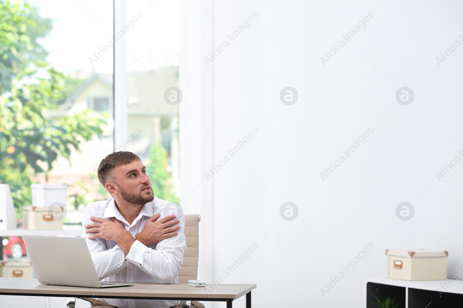 Photo of Young man suffering from cold in office. Air conditioner malfunction