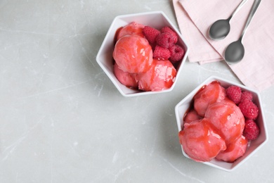 Photo of Delicious pink ice cream with raspberries in bowls on grey marble table, flat lay. Space for text