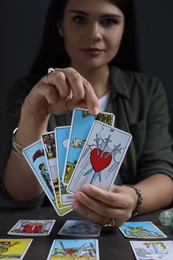 Fortune teller with tarot cards at grey table indoors, focus on hands