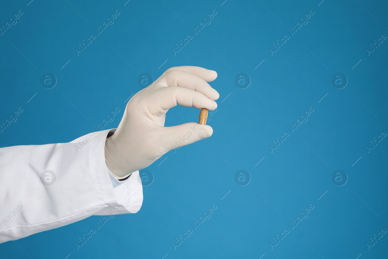 Photo of Doctor holding suppository for hemorrhoid treatment on blue background, closeup