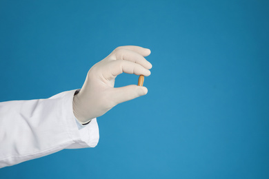 Photo of Doctor holding suppository for hemorrhoid treatment on blue background, closeup