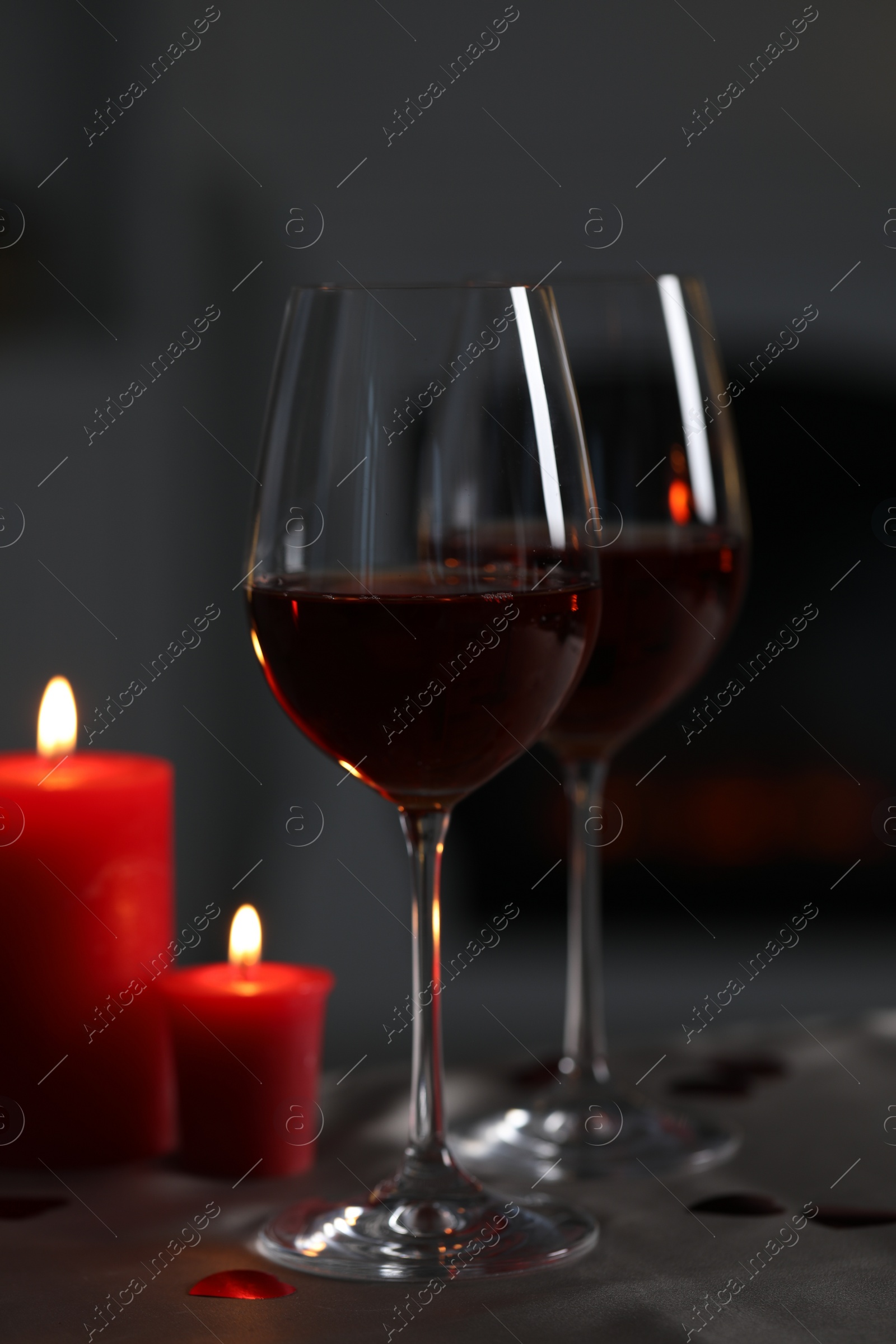 Photo of Glasses of red wine and burning candles on grey table against blurred background. Romantic atmosphere