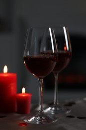 Photo of Glasses of red wine and burning candles on grey table against blurred background. Romantic atmosphere