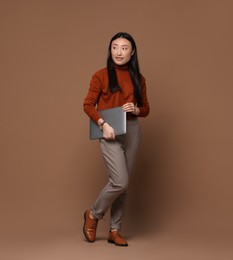 Photo of Full length portrait of smiling woman with laptop on brown background. Space for text