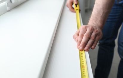 Man measuring white windowsill indoors, closeup view with space for text. Construction tool