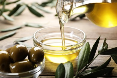 Pouring olive oil from jug into bowl on wooden table, closeup. Healthy cooking