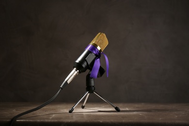 Photo of Microphone with purple awareness ribbon on wooden table against dark background