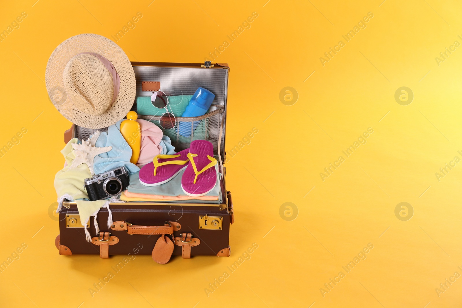 Photo of Packed vintage suitcase with different beach objects on orange background, space for text. Summer vacation