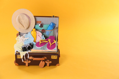 Photo of Packed vintage suitcase with different beach objects on orange background, space for text. Summer vacation