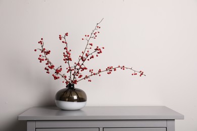 Photo of Hawthorn branches with red berries in vase on grey table indoors, space for text