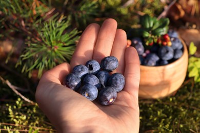 Photo of Woman holding heap of fresh ripe blueberries in forest, closeup