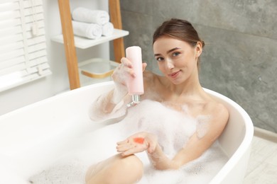 Woman pouring shower gel onto hand in bath indoors