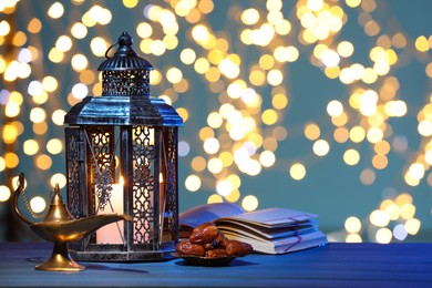 Photo of Arabic lantern, Quran, dates and Aladdin magic lamp on table against light blue background with blurred lights. Space for text
