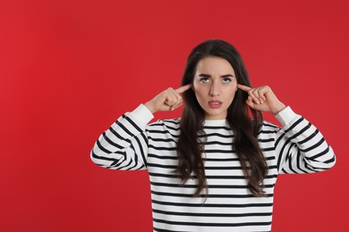 Photo of Young woman covering ears with fingers on red background