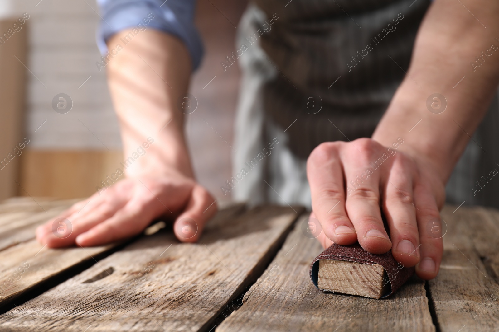 Photo of Man polishing wooden table with sandpaper indoors, closeup