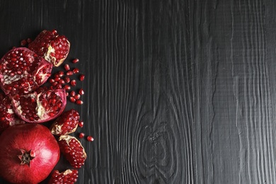 Photo of Ripe pomegranates on dark wooden background, top view with space for text