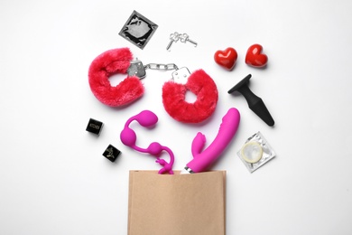 Photo of Paper shopping bag with different sex toys on white background, top view