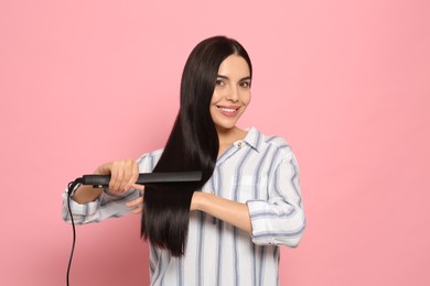 Photo of Beautiful happy woman using hair iron on pink background
